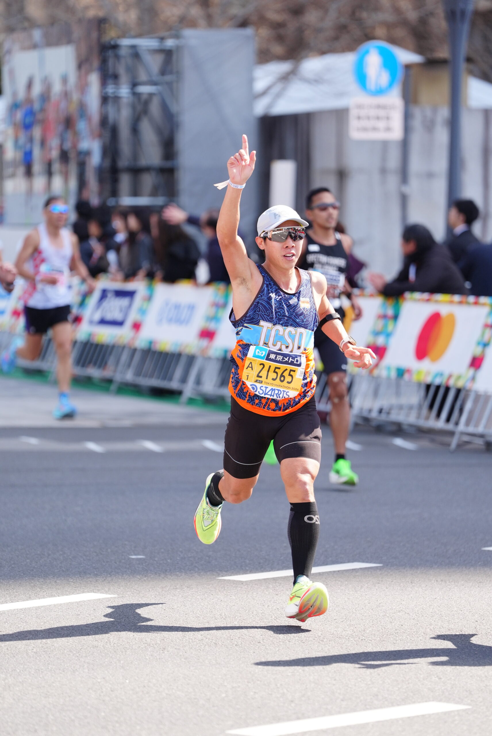 Anthony racing at the Tokyo Marathon, wearing bib number 21565, arm raised in celebration
